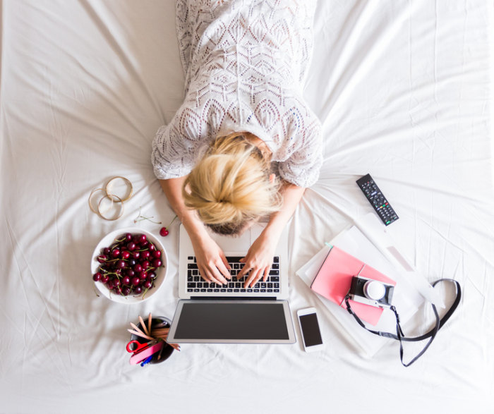 femme couchée sur un lit tapant sur son clavier d'ordinateur